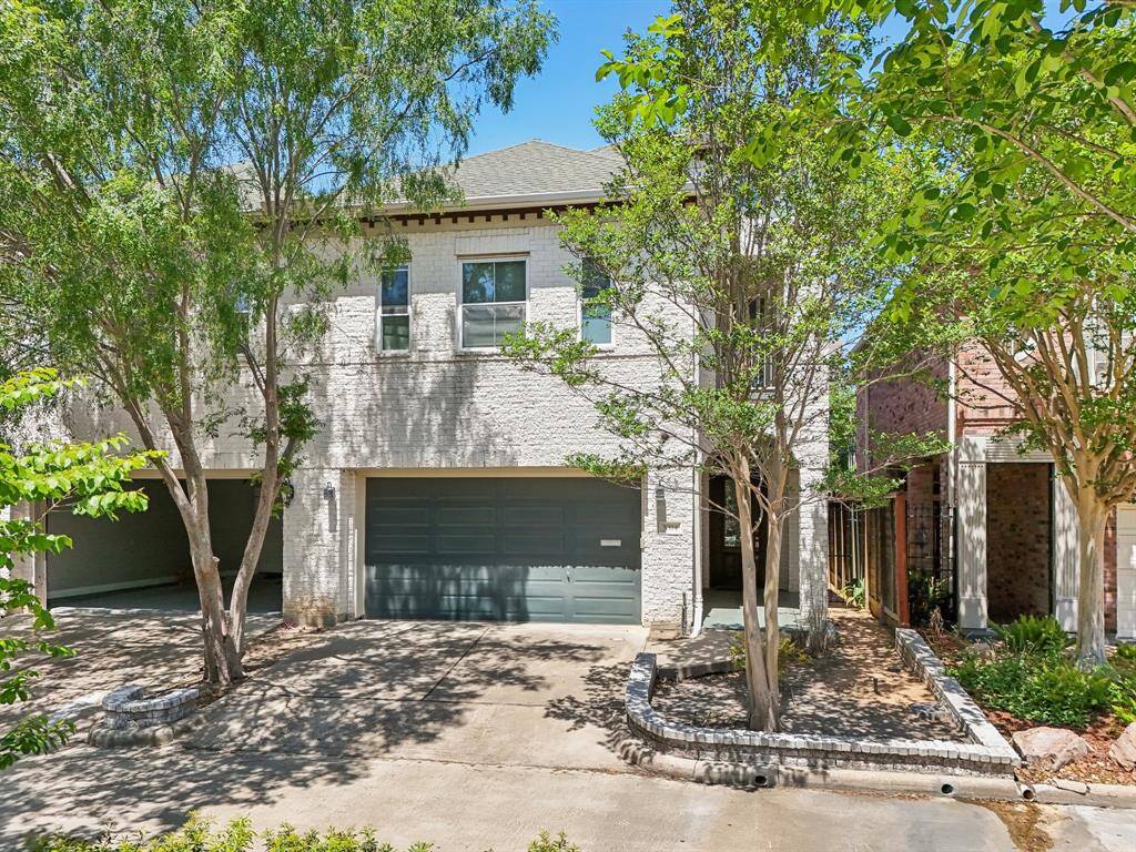 Modern three-story home with a light brick exterior and a two-car garage. The property is surrounded by mature trees, providing shade and adding to the curb appeal. The driveway and walkway are well-maintained, enhancing the welcoming appearance.