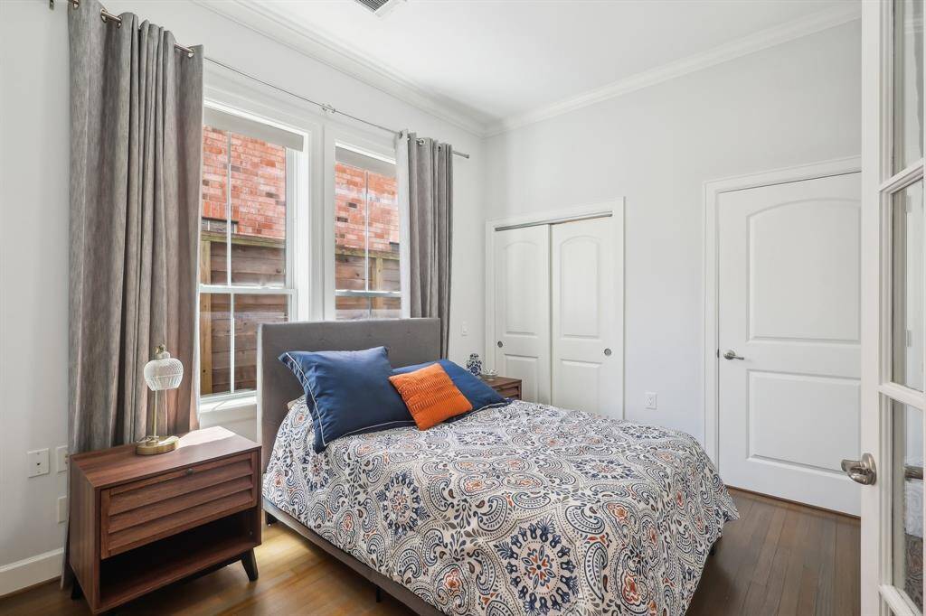 This cozy downstairs room has large windows with elegant curtains and a closet with double doors. Neutral walls and wood flooring create a warm, inviting atmosphere.