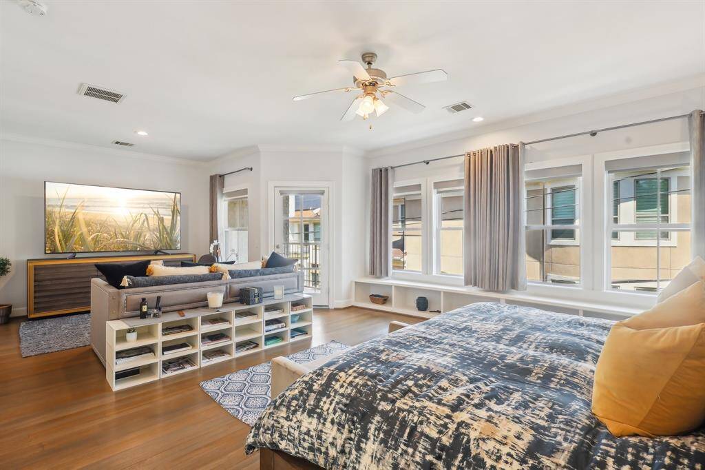Another view of the spacious primary bedroom suite with large windows and ample natural light.  The room has a modern, airy feel with wood flooring.