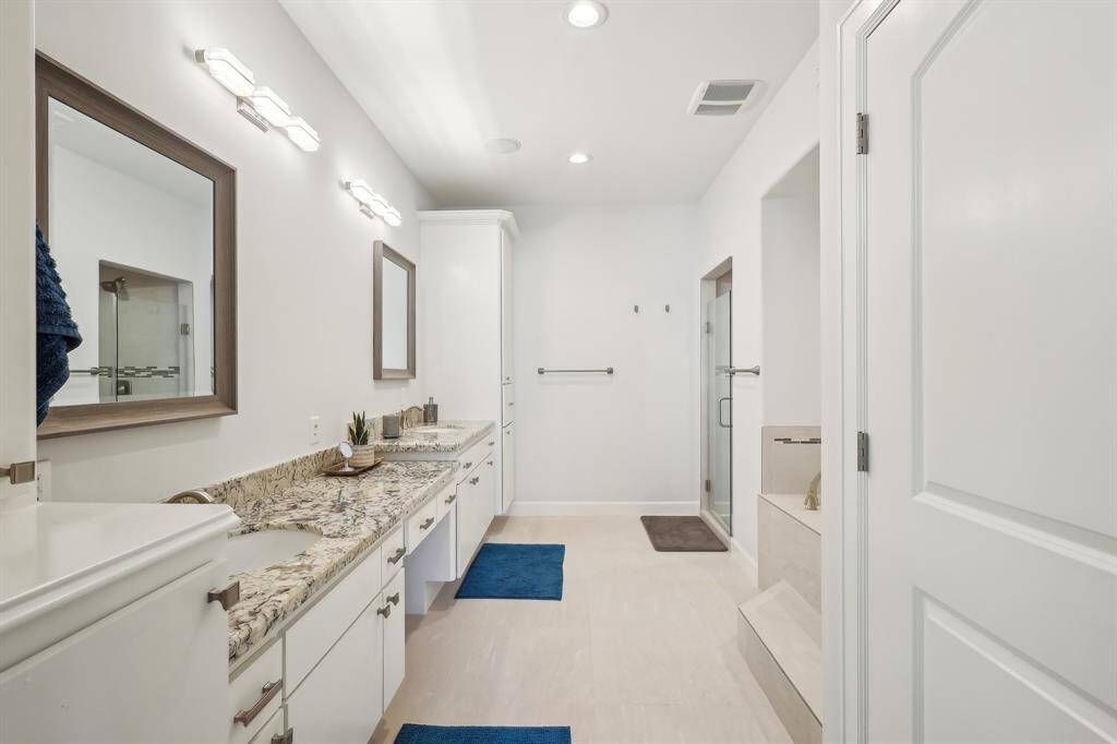 Primary suite bathroom features a dual-sink vanity with granite countertops, modern fixtures, and ample storage. It includes a glass-enclosed shower, garden tub and neutral tile flooring, offering a clean, contemporary look.
