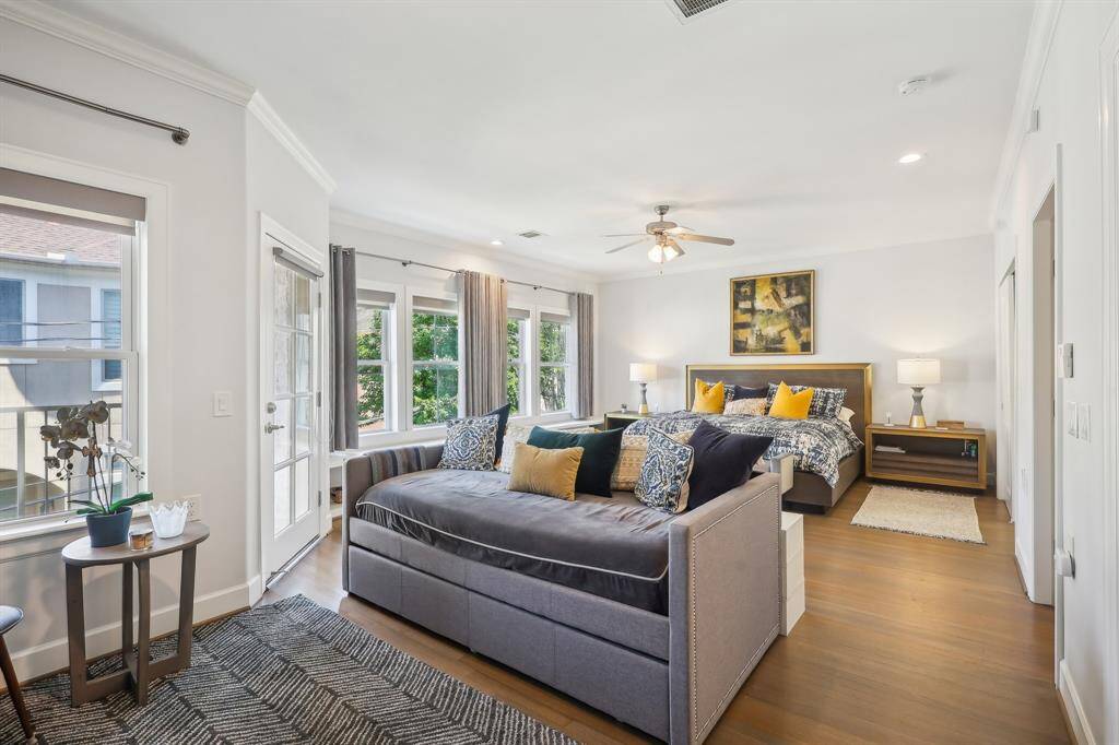 The spacious primary bedroom features abundant natural light and a cozy seating area.  The room includes a ceiling fan, hardwood floors, and access to a private balcony.