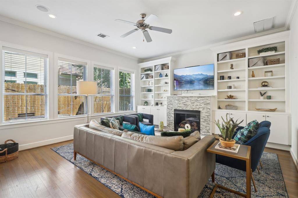 This inviting living room features large windows for ample natural light, built-in shelves, a cozy fireplace, and a modern ceiling fan, creating a perfect space for relaxation and entertainment.