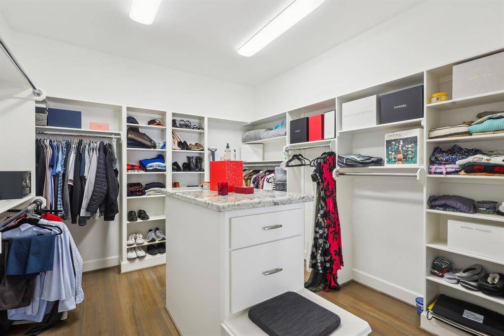 This spacious primary suite, walk-in closet features built-in shelves and hanging space for clothes, shoes, and accessories. It has a central island with drawers and is well-lit, providing ample storage and organization.