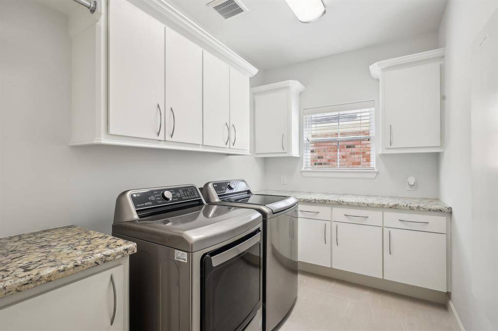 Bright, modern laundry room is on second floor. It has ample storage with white cabinets and granite countertops, complemented by a window allowing natural light.