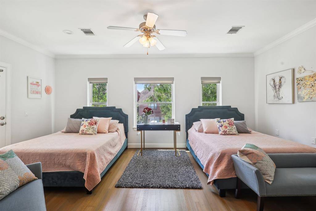This spacious bedroom features a ceiling fan, ample natural light from three windows, and a cozy seating area, creating a serene and inviting atmosphere.