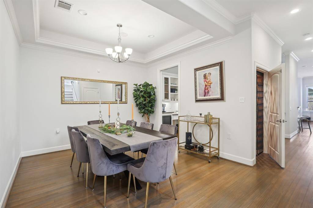 This formal dining room features elegant hardwood flooring, a modern chandelier, and has space for a table with seating for eight.