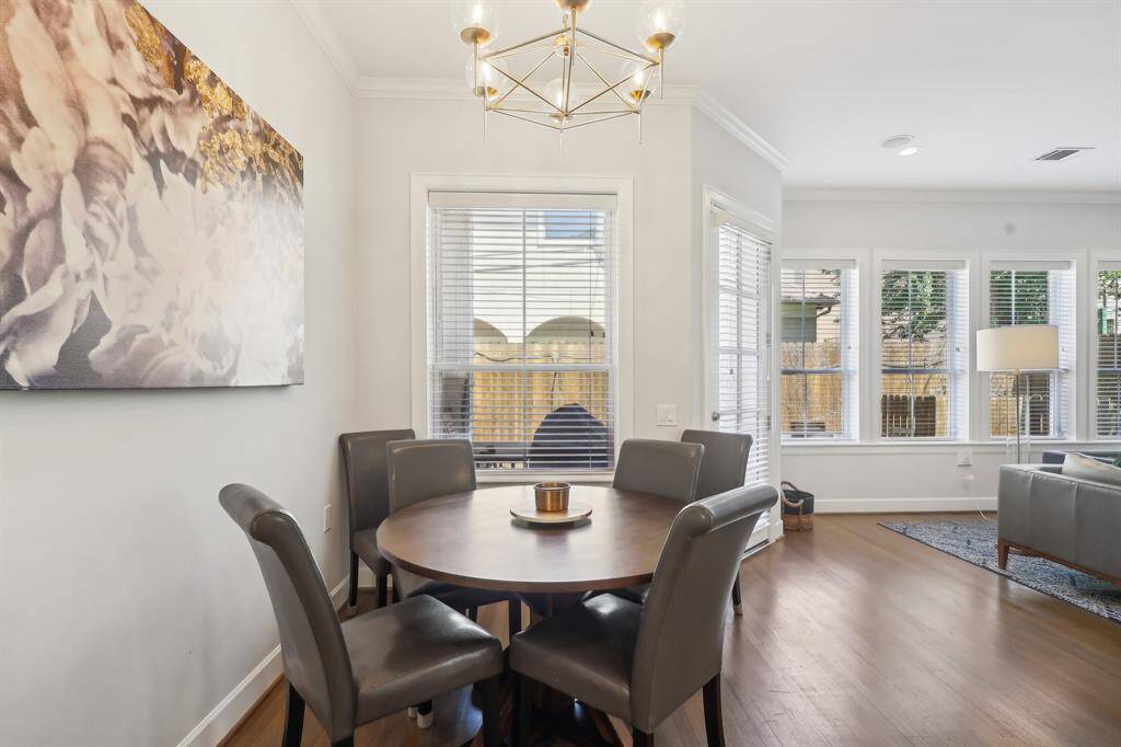 Bright breakfast dining area featuring large windows that provide natural light. The space is open to a cozy living area, showcasing hardwood floors and modern decor.