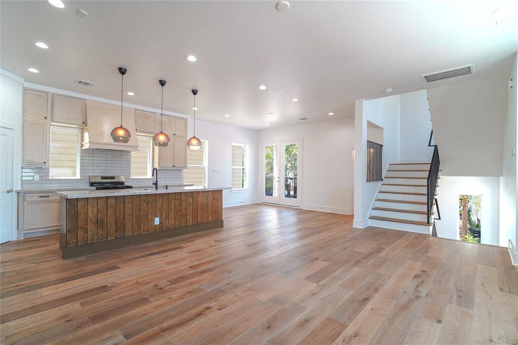 This modern living space features an open layout with large windows, ample natural light, and a neutral color palette. The living room flows into a dining area and kitchen with contemporary lighting and sleek finishes, offering a welcoming and stylish environment.