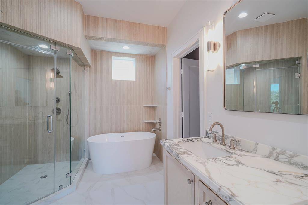 The Primary Bathroom features a double vanity with natural stones, a standing shower with custom built tiles all around and a modern soaking tub.
