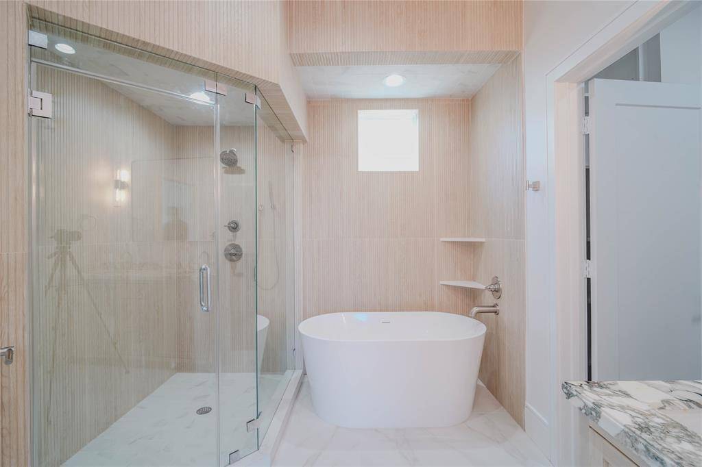 The Primary Bathroom features a double vanity with natural stones, a standing shower with custom built tiles all around and a modern soaking tub.