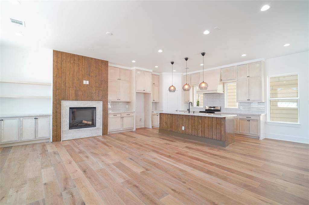This modern living space features an open layout with large windows, ample natural light, and a neutral color palette. The living room flows into a dining area and kitchen with contemporary lighting and sleek finishes, offering a welcoming and stylish environment.