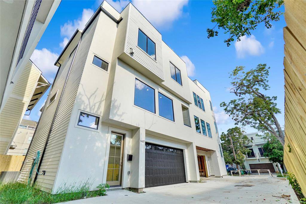 *Photos are from 5435 Darling* Modern three-story home with a sleek stucco exterior, featuring a large garage door, balcony, and minimalist landscaping. Located in a cozy neighborhood with a wooden privacy fence and mature trees.