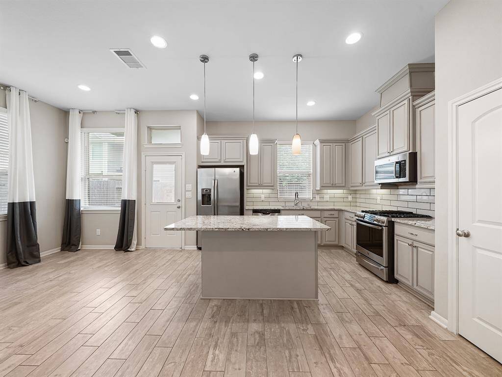 The kitchen is a culinary dream, featuring sleek stainless steel appliances for modern convenience. Designer touches include elegant pendant and under-counter lighting, complemented by a stylish glass tile backsplash. Upgraded glazed cabinets provide ample storage space, enhancing both functionality and aesthetic appeal.