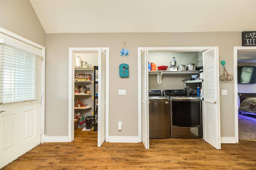 This photo shows  utility space with a walk-in pantry on the left and a laundry area on the right, featuring modern appliances. The room has neutral flooring and neutral walls, providing a clean and organized look.