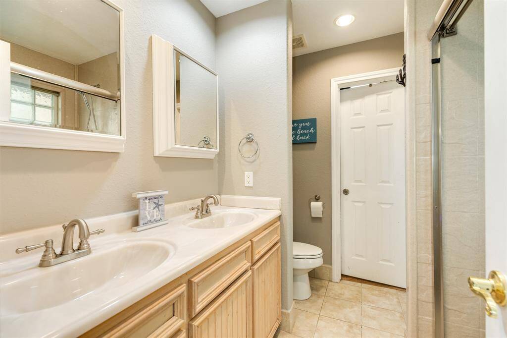 This bathroom features a dual-sink vanity with elegant fixtures, a large mirror, and ample storage. Neutral tones create a calming atmosphere, while the tiled floor and shower enclosure add a touch of luxury.