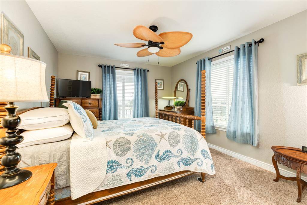 3rd bedroom with beach-themed decor, featuring a ceiling fan, light blue curtains, and a comfortable bed. The room is bright and inviting, with two windows providing ample natural light.