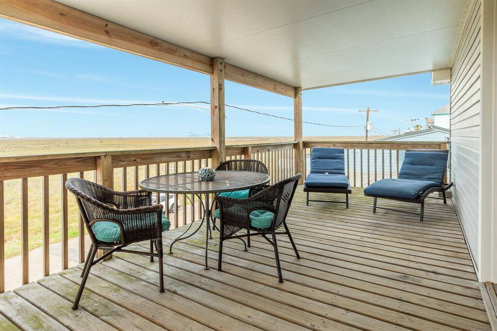 This photo shows the spacious, covered wooden back deck with a seating area, including a round table and cushioned chairs. It offers expansive views of open bay views, perfect for relaxation and outdoor enjoyment.