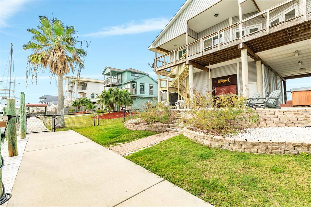 This canal front property features an elevated, modern home with spacious decking, a hot tub, and a well-maintained yard. It offers easy access to the water, surrounded by lush greenery and neighboring homes, creating a serene coastal living environment.