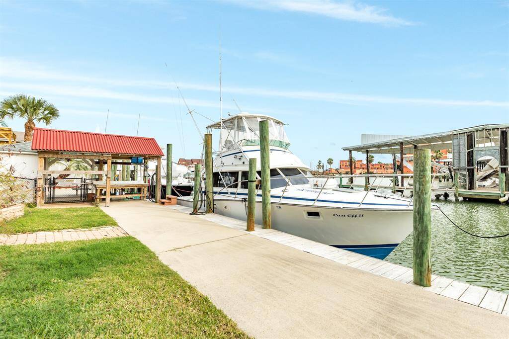 56 Marlin is a canal front property with a private dock, featuring a boat moored beside a well-maintained path. The setting includes a covered fishing station with a red roof and lush green lawn, ideal for boating enthusiasts.