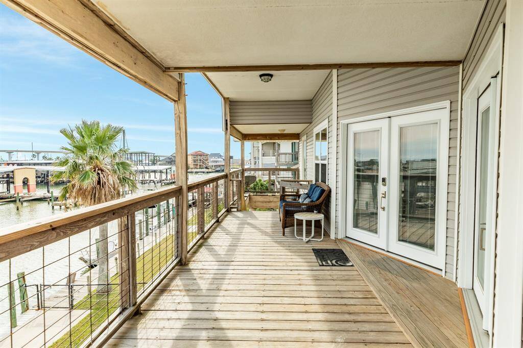 This photo shows a spacious wooden deck with a waterfront view, featuring two wicker chairs and a small table and offers access through elegant French doors, perfect for relaxing and enjoying the serene surroundings.