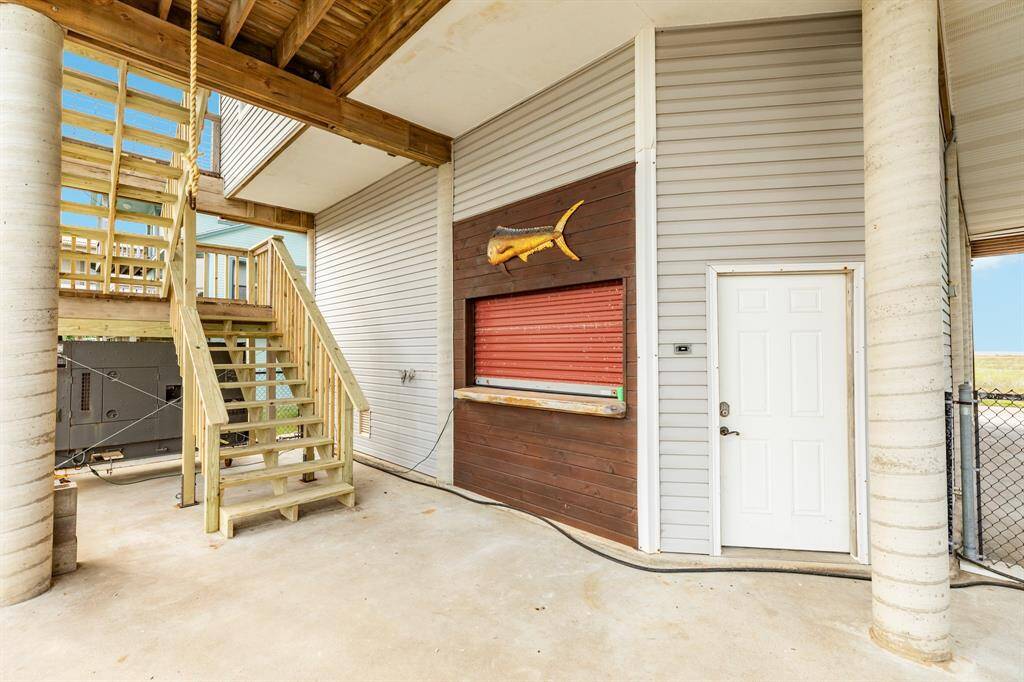 Outdoor bar area under the covered patio. There are recently installed wooden stairs leading to an upper level, a door to an enclosed space, and a decorative fish mounted on the siding. The area has a coastal, rustic charm.