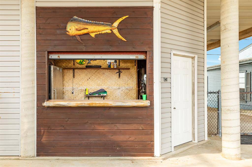 This photo showcases an outdoor bar area with a wooden facade, featuring a fish decoration. It includes a serving counter with a backsplash and a nearby door leading into the garage ideal for entertaining.