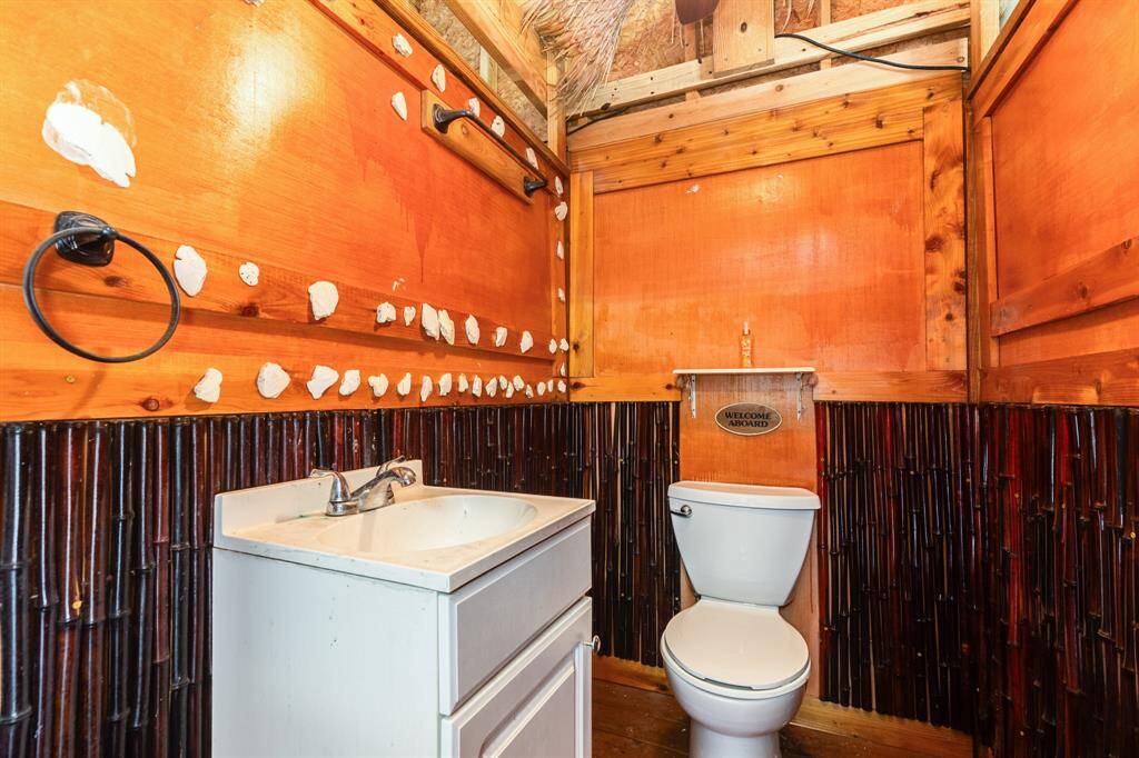 This ground floor half bath features a rustic design with wood paneling and unique decorative accents. It includes a white sink with storage and a toilet, creating a cozy, cabin-like atmosphere.