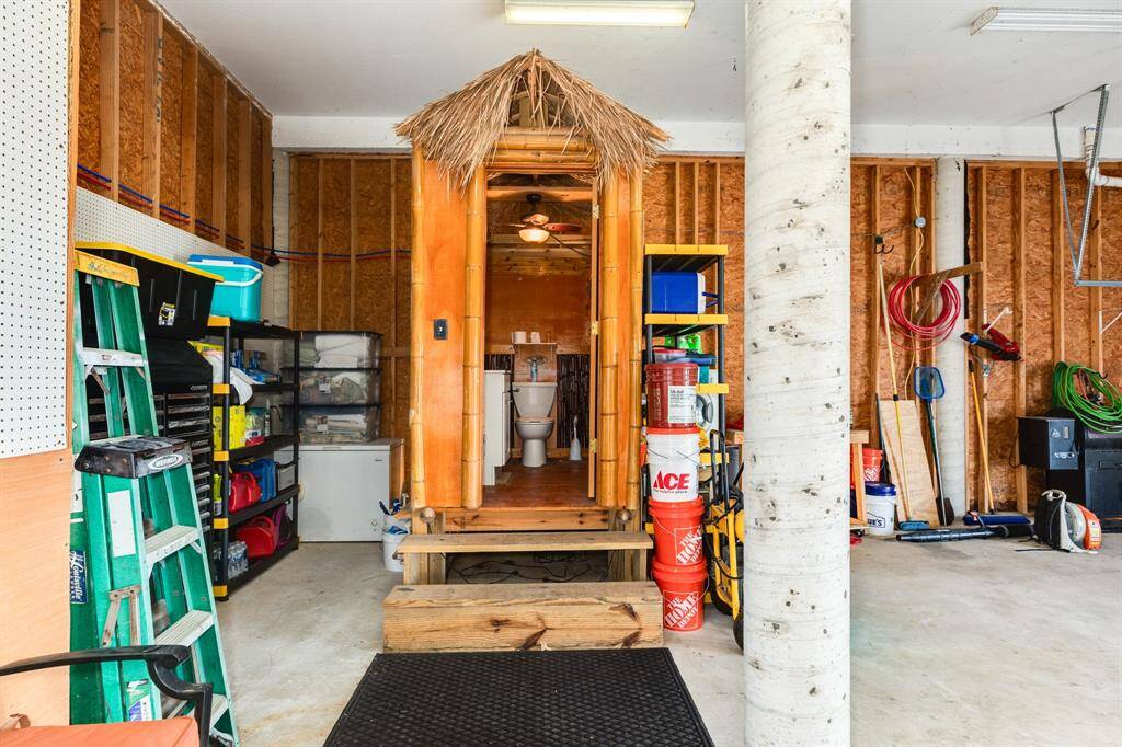 This photo showcases a garage  ample storage space, and a unique tiki-style half bath. The area includes shelves, ladders, and tools, offering practical functionality.