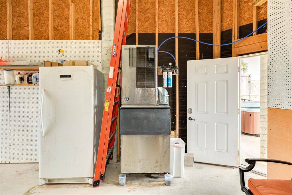 The ground floor includes an ice maker and additional freezer in the garage or workshop, featuring pegboard walls,. There's an open door leading outside, and some storage shelves with various items. The space is functional and organized.