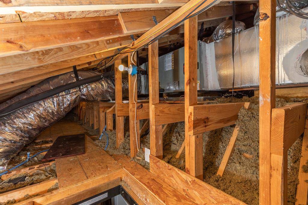 This photo shows a well-maintained attic space with visible insulation, wooden framing, and ductwork and recently installed HVAC unit.