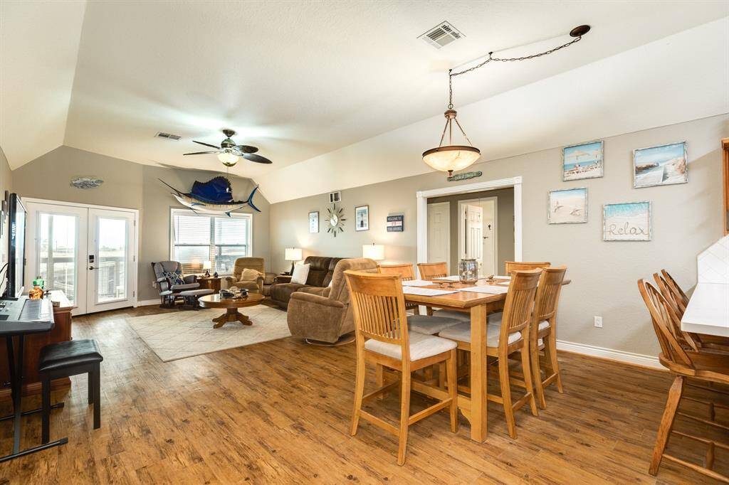 This spacious open-concept living and dining area features warm wood flooring, neutral walls, and ample natural light. It includes a cozy seating area, dining table, and a bar-style counter, perfect for entertaining. Decorated with coastal-themed accents, it offers a relaxed, inviting atmosphere.