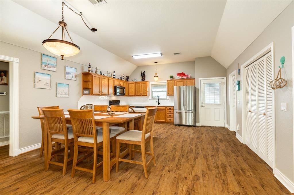 This inviting kitchen features warm wooden cabinetry, stainless steel finish appliances, and a spacious dining area with a modern light fixture. The open layout and vaulted ceiling enhance the airy feel, ideal for gatherings.