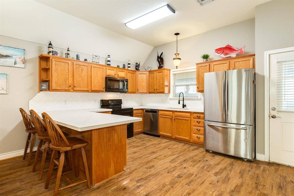 This bright kitchen features cabinets, modern stainless steel finish appliances, and a large island with bar seating. The flooring adds warmth, and spacious counter space makes it ideal for cooking and entertaining.