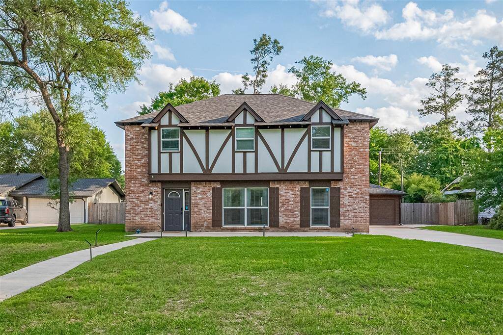 This photo features a charming two-story brick house with Tudor-style accents. It has an amazing front lawn! Set in a serene neighborhood with mature trees and beautiful quarter up to half acre lots!