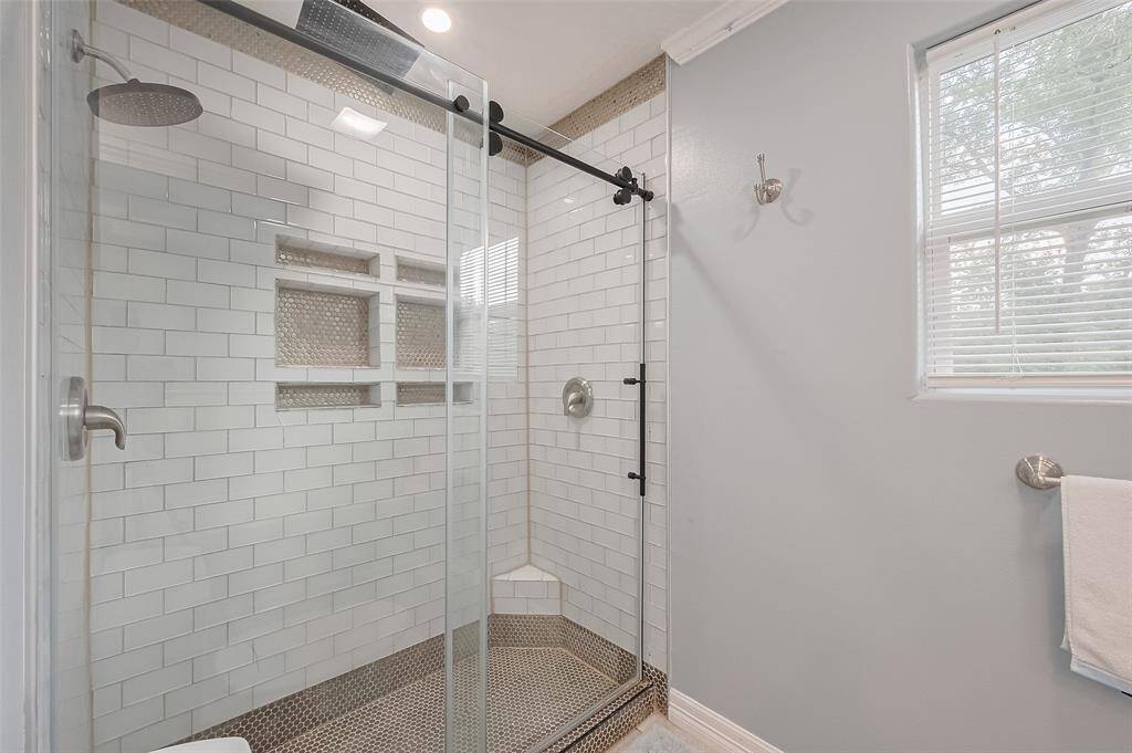 Modern bathroom with a updated walk-in shower featuring a sliding glass door, subway tile walls, and built-in shampoo nooks. Natural light streams in through a nearby window, highlighting the sleek fixtures and clean design.