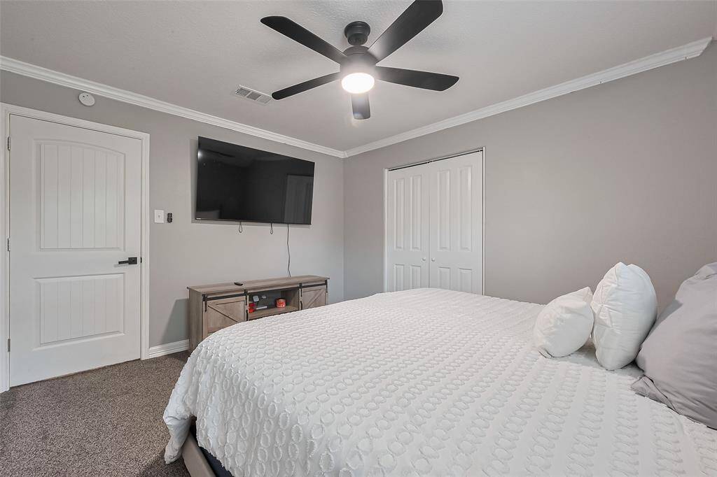 This bedroom features soft gray walls, a modern ceiling fan, double-door closet and carpeted flooring, creating a cozy and contemporary space.