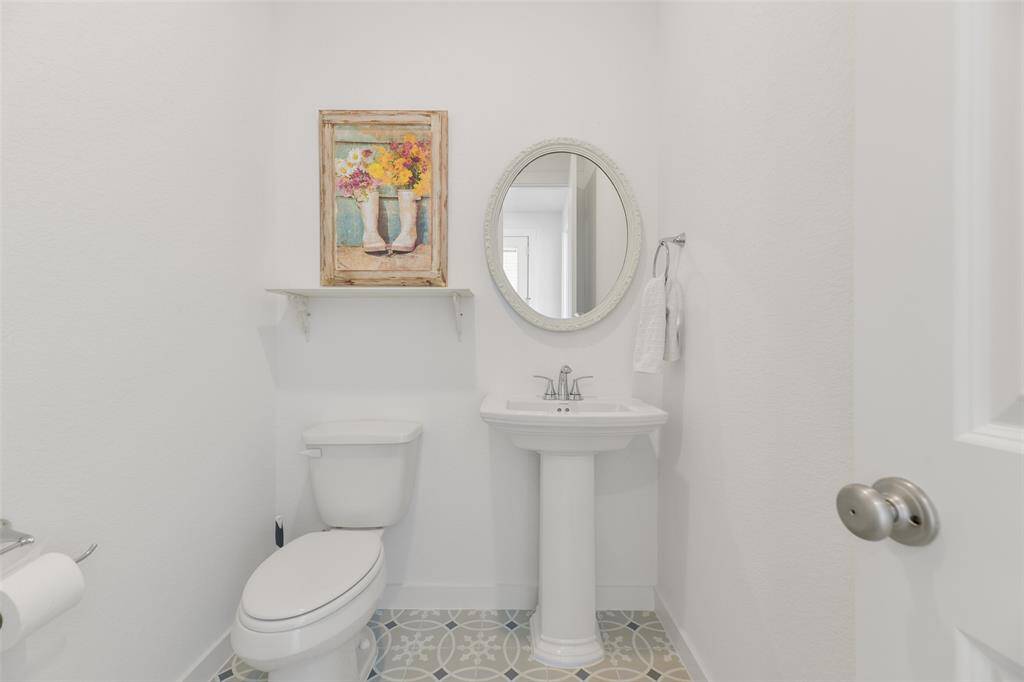 This half bathroom serviced house guests and it offers a simple pedestal sink topped by an oval-shaped framed mirror surrounded by neutral paint and a pop of color from the designer tile on the floor.