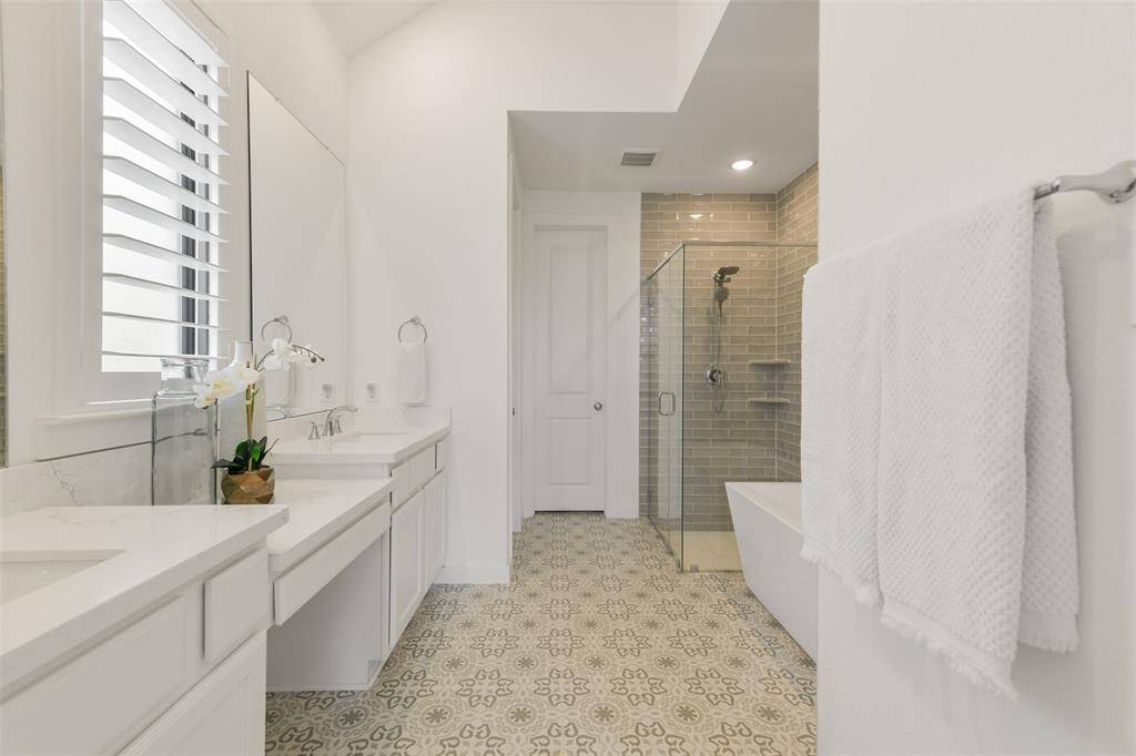 Relaxation awaits in this spa-worthy private bath with a seated vanity, his & hers rectangular basin sinks with quartz countertops, white cabinetry, designer tile flooring, a freestanding soaker tub, & an oversized seamless glass shower with a grey glass subway tile surround.