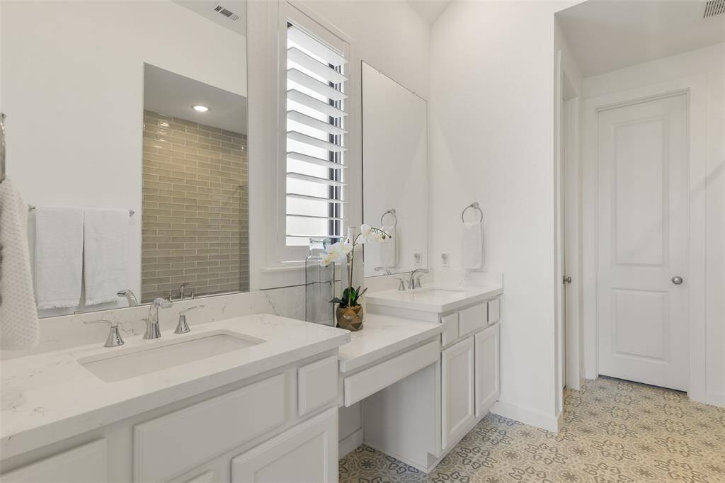 Relaxation awaits in this spa-worthy private bath with a seated vanity, his & hers rectangular basin sinks with quartz countertops, white cabinetry, designer tile flooring, a freestanding soaker tub, & an oversized seamless glass shower with a grey glass subway tile surround.