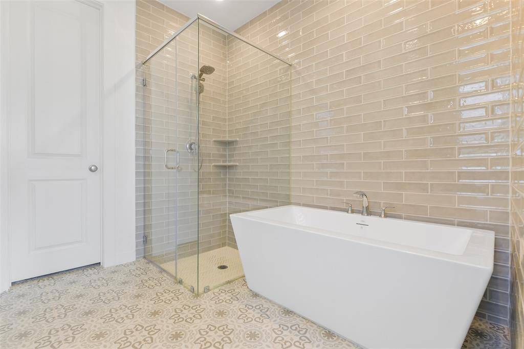 Relaxation awaits in this spa-worthy private bath with a seated vanity, his & hers rectangular basin sinks with quartz countertops, white cabinetry, designer tile flooring, a freestanding soaker tub, & an oversized seamless glass shower with a grey glass subway tile surround.