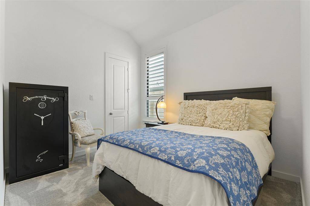 The first of three secondary bedrooms in this home offers a raised gambrel ceiling, a side facing window dressed with plantation shutters, plush carpet underfoot, and a walk-in closet.