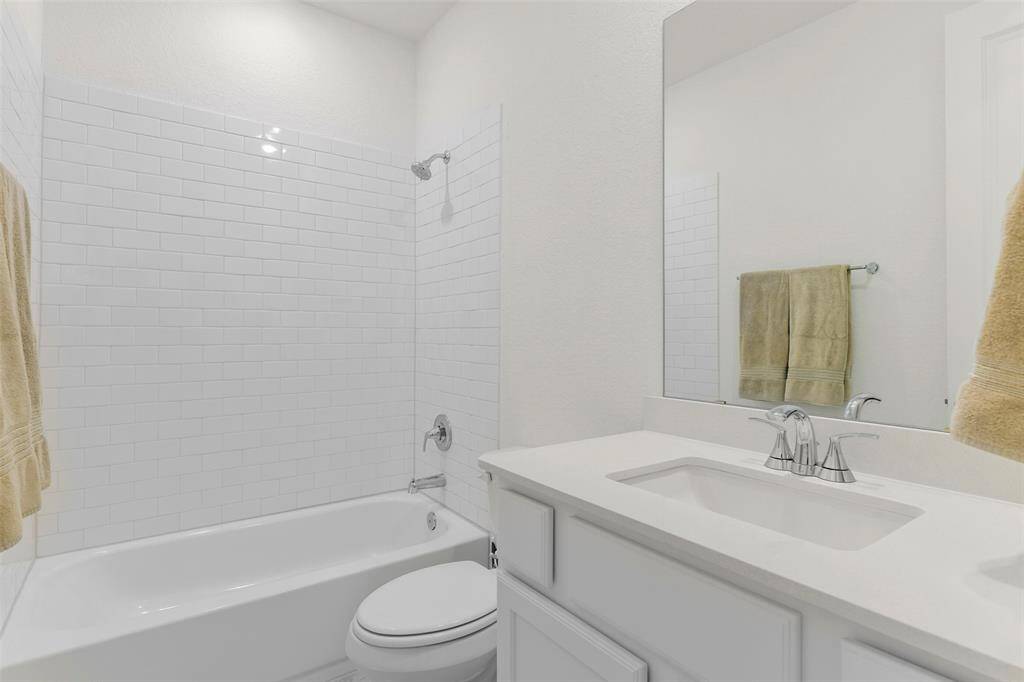 In this bathroom, find a gleaming quartz top vanity with an undermount rectangular basin sink, a polished chrome faucet, white cabinetry, tile floors, and a combination bathtub and shower with a timeless subway tile backsplash.