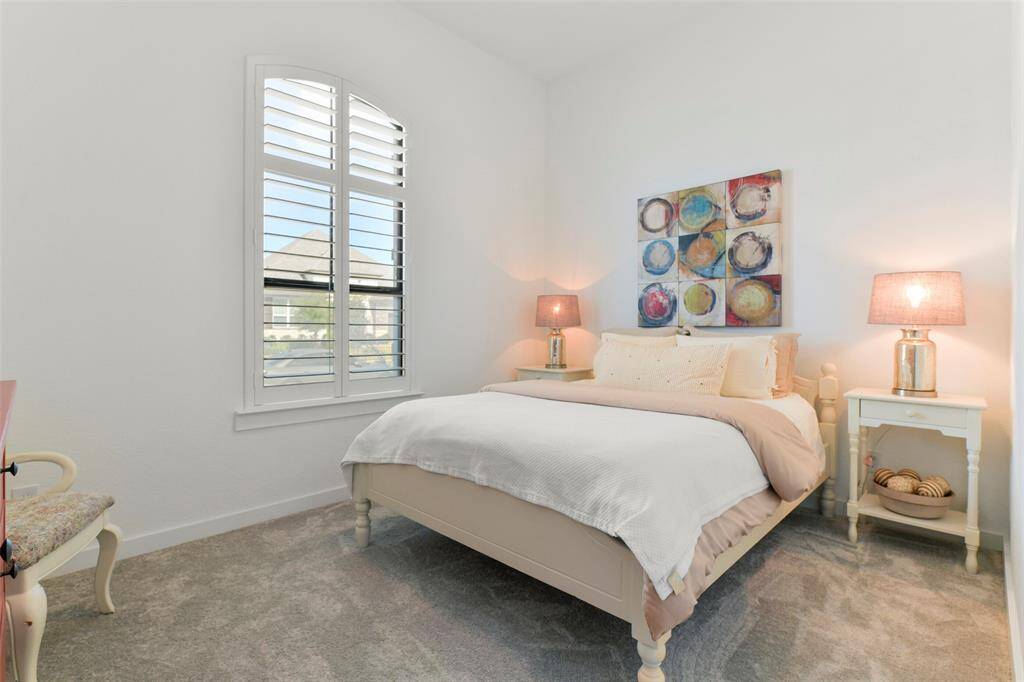 Another secondary bedroom is similar in size and features to the previous room, also featuring an elevated ceiling, plush carpet, a walk-in closet, and a front-facing palladium arched window with plantation shutters. This bedroom boasts an en suite bathroom as well.