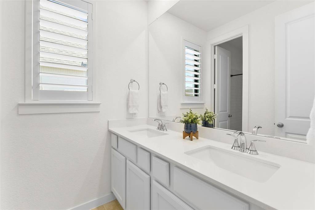 To service multiple rooms and people, this bathroom offers a lengthy quatyz top vanity with dual rectangular basin sinks, polished chrome faucets, white cabinetry, tile floors, and a combination bathtub and shower with a subway tile surround.