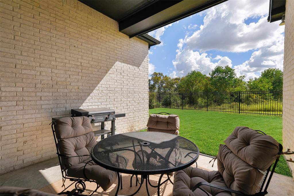 Step outdoors from the main living area onto this ample covered patio with recessed lights, a concrete floor, and views of the compact backyard with a wrought iron fence and peaceful park-like greenspace beyond.