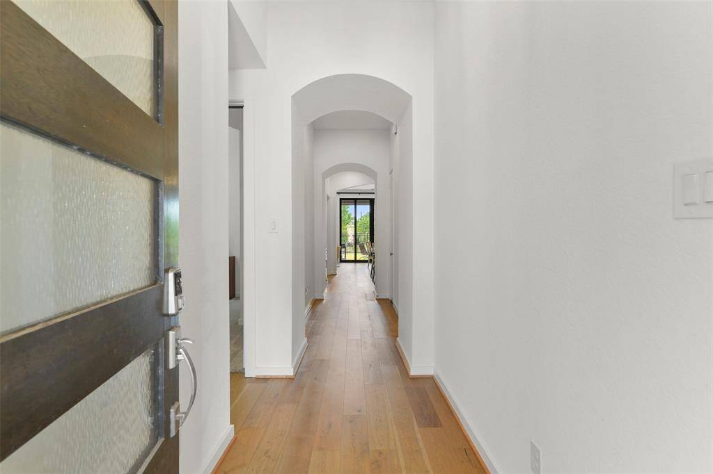 The modern-style front door with frosted glass panels opens to reveal a lengthy hallway with elevated ceilings, graceful arched doorways, neutral paint, engineered wood floors, and views all the way to the back of the home and beyond.