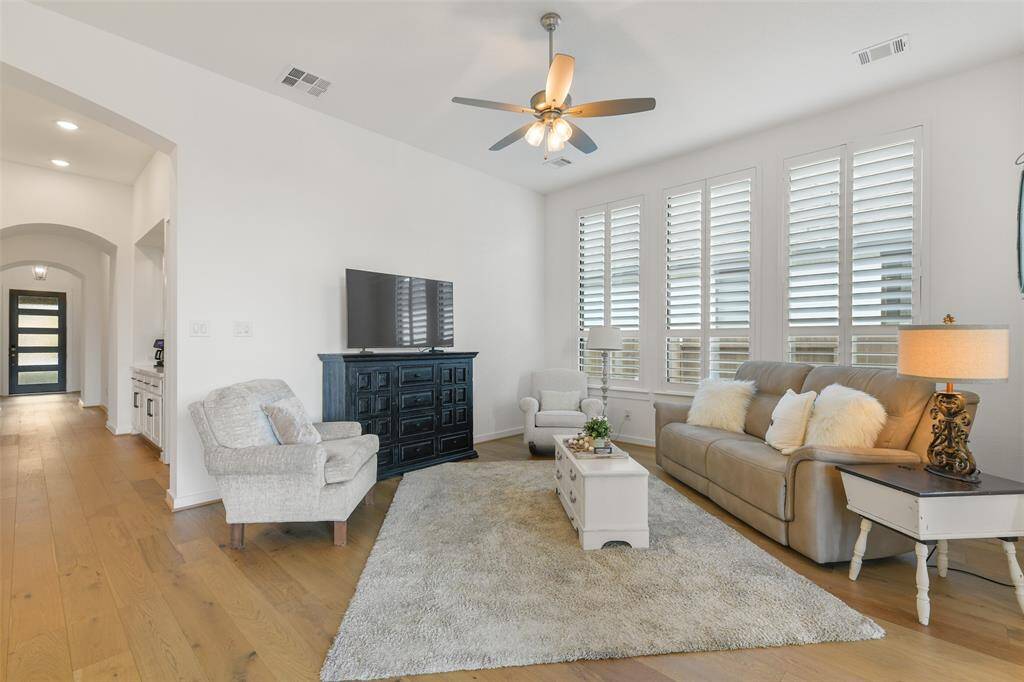 The main hallway extends past the secondary bedrooms at the front of the home, as well as a built-in buffet or beverage station, to land in this comfortable and inviting family room with high ceilings, a lighted ceiling fan, and a wall of windows shaded by timeless plantation shutters.