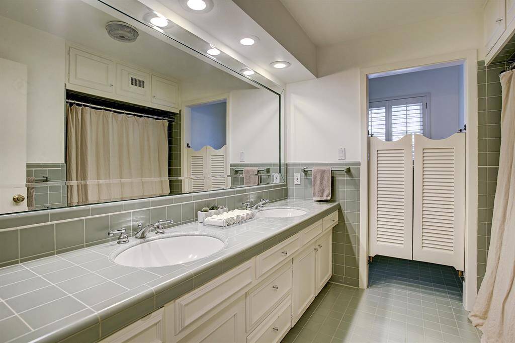 Hall bathroom with double sinks & tub with shower. Sparkling tile on counters & floor.
