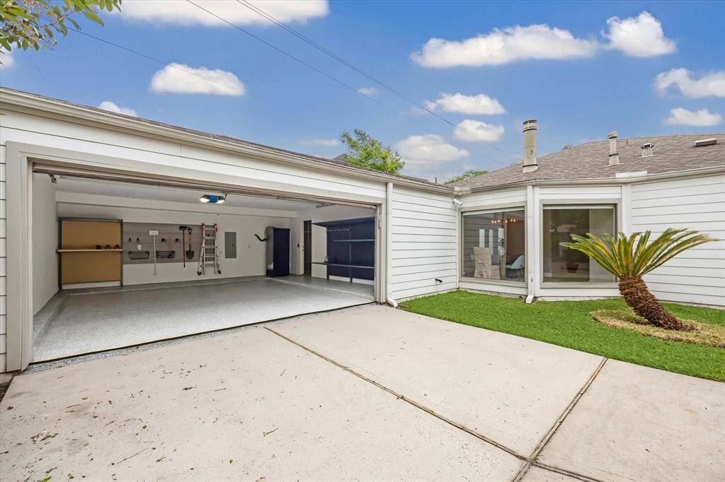 A view of the clean, well-organized garage featuring a durable epoxy floor finish. The extended driveway offers ample parking for multiple vehicles, providing plenty of space for both residents and guests.