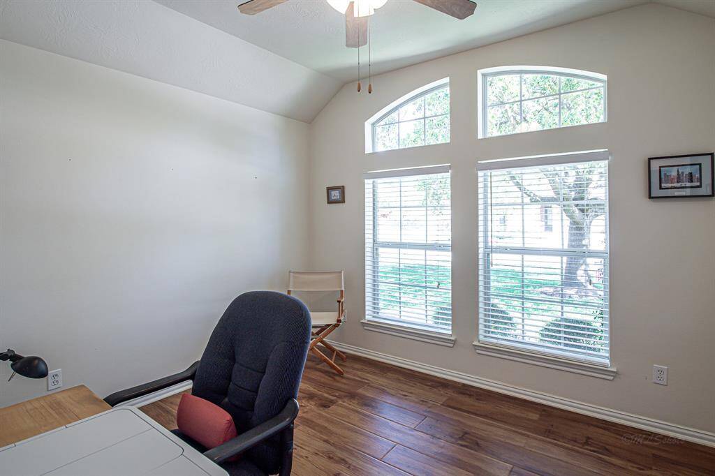 The secondary bedroom features elegant flooring and tall ceilings, offering a bright view of the front yard's mature shade tree.